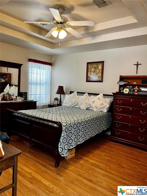 bedroom featuring a textured ceiling, hardwood / wood-style flooring, ceiling fan, and a raised ceiling