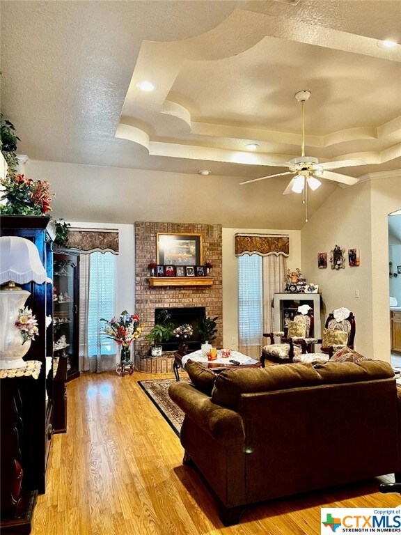 4305 Foster Ln, Killeen, TX 76549 - living area featuring a raised ceiling, a fireplace, a ceiling fan, light wood finished floors, and a textured ceiling