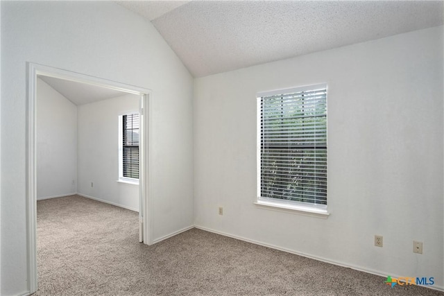 empty room with a textured ceiling, lofted ceiling, and light carpet