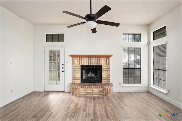 unfurnished living room featuring a brick fireplace, ceiling fan, light wood-type flooring, a textured ceiling, and a towering ceiling