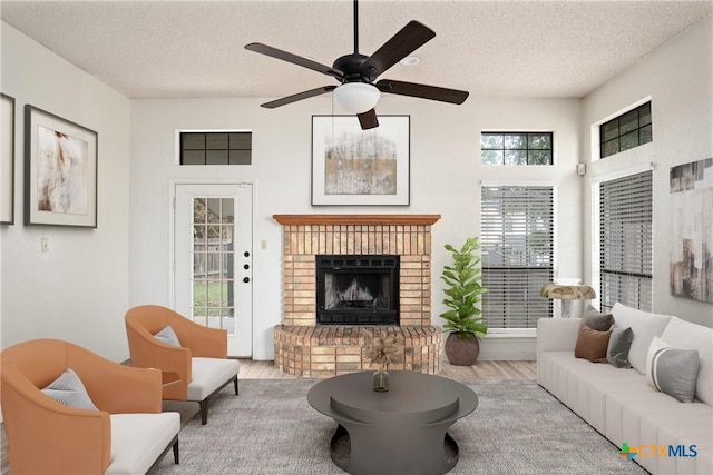 living room featuring light hardwood / wood-style flooring, a healthy amount of sunlight, a textured ceiling, and a brick fireplace