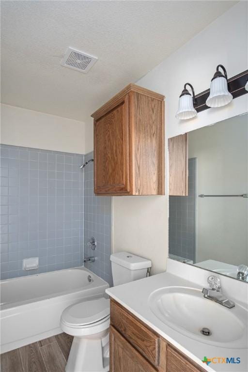 full bathroom featuring tiled shower / bath combo, hardwood / wood-style floors, a textured ceiling, toilet, and vanity