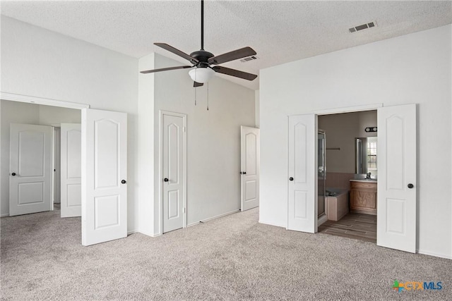 unfurnished bedroom featuring a textured ceiling, ceiling fan, ensuite bathroom, and light carpet