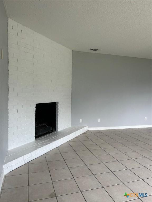 unfurnished room featuring a textured ceiling, visible vents, a brick fireplace, light tile patterned floors, and baseboards