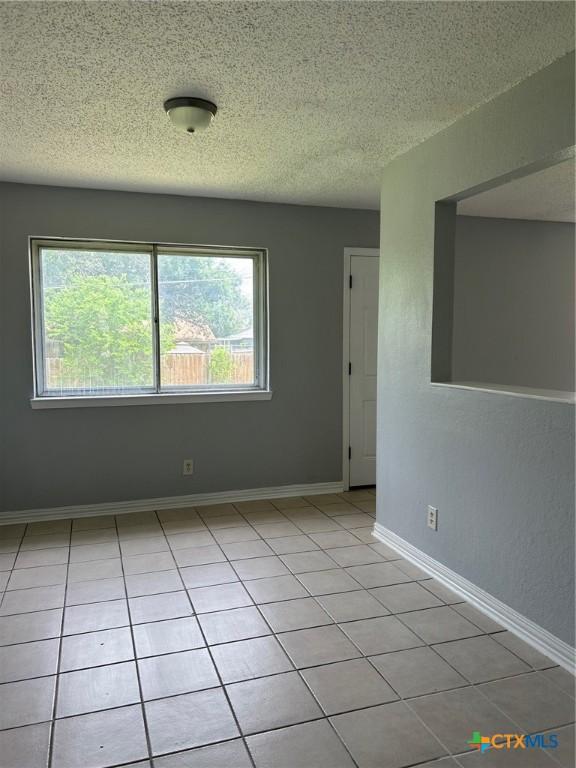 empty room featuring baseboards, light tile patterned flooring, and a textured ceiling