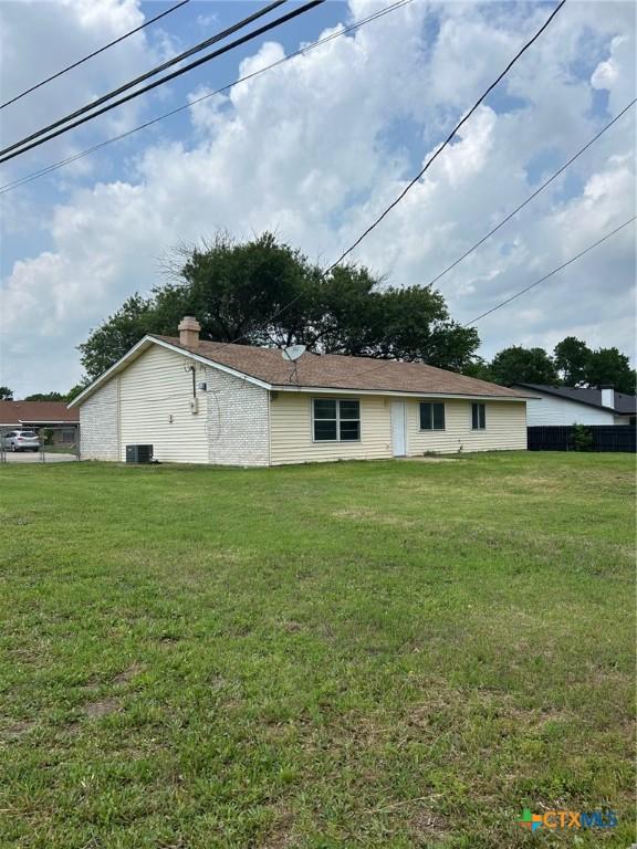 rear view of property with central AC unit, a chimney, and a yard