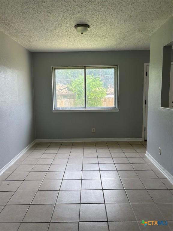 unfurnished room featuring light tile patterned floors, baseboards, and a textured ceiling
