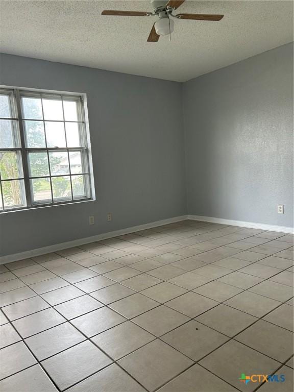 spare room with a ceiling fan, a textured ceiling, light tile patterned floors, and baseboards