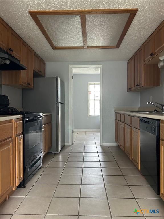 kitchen with a sink, light countertops, black appliances, under cabinet range hood, and light tile patterned flooring