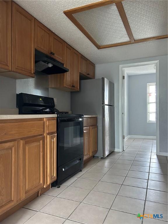 kitchen with light tile patterned flooring, black gas range oven, light countertops, brown cabinetry, and under cabinet range hood