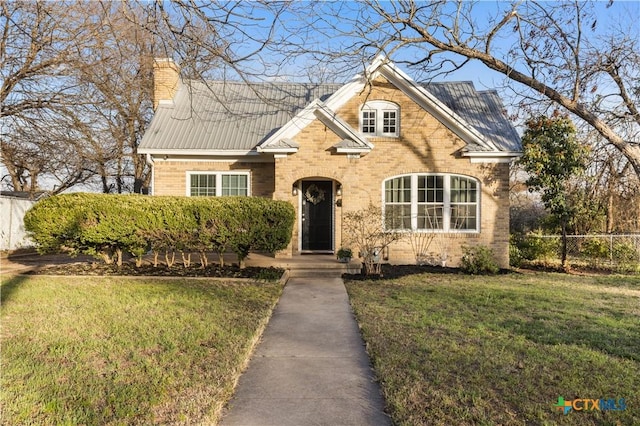 traditional-style house with brick siding, a chimney, a front yard, metal roof, and fence