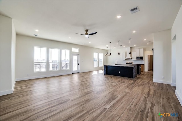 unfurnished living room featuring ceiling fan, plenty of natural light, wood-type flooring, and sink