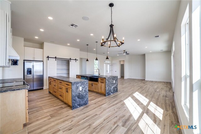 kitchen with pendant lighting, stainless steel refrigerator with ice dispenser, a barn door, light hardwood / wood-style floors, and white cabinetry