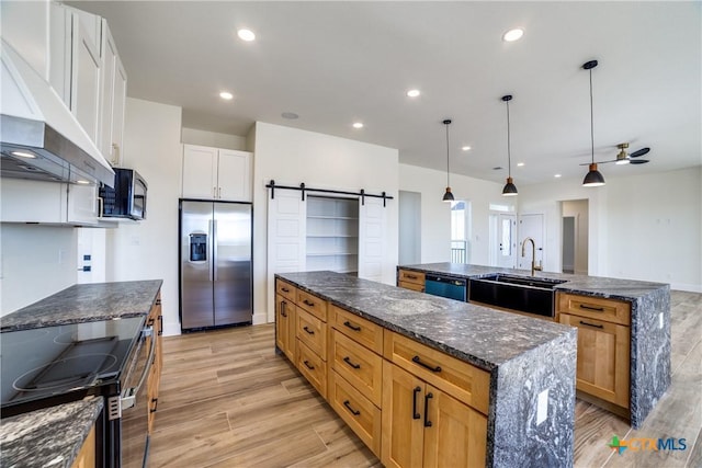 kitchen featuring pendant lighting, black appliances, white cabinets, a barn door, and light hardwood / wood-style floors