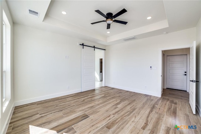 unfurnished room with light wood-type flooring, a barn door, a tray ceiling, and ceiling fan