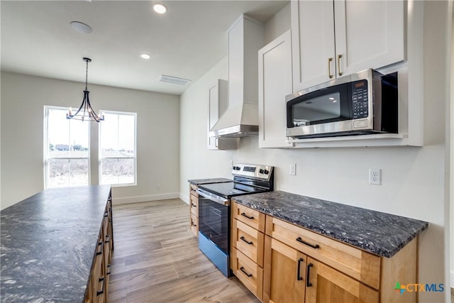 kitchen with dark stone counters, stainless steel appliances, white cabinets, light hardwood / wood-style floors, and hanging light fixtures