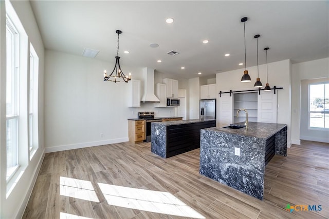 kitchen featuring white cabinetry, sink, wall chimney exhaust hood, a barn door, and a kitchen island with sink