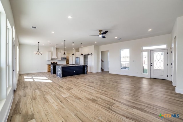 unfurnished living room featuring ceiling fan with notable chandelier, light hardwood / wood-style flooring, and sink