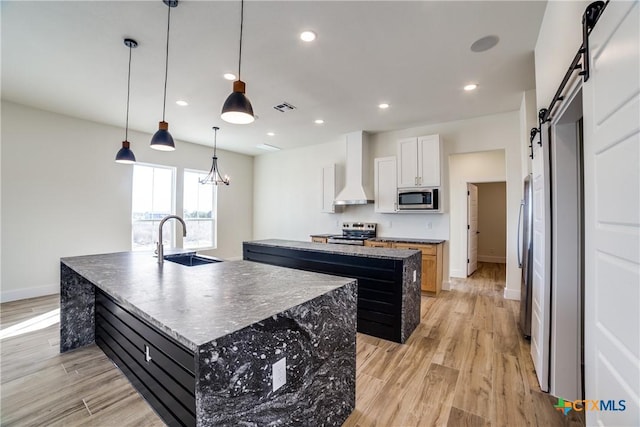 kitchen featuring a kitchen island with sink, white cabinets, sink, a barn door, and stainless steel appliances