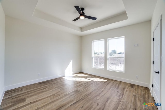 empty room with a raised ceiling, ceiling fan, and light wood-type flooring