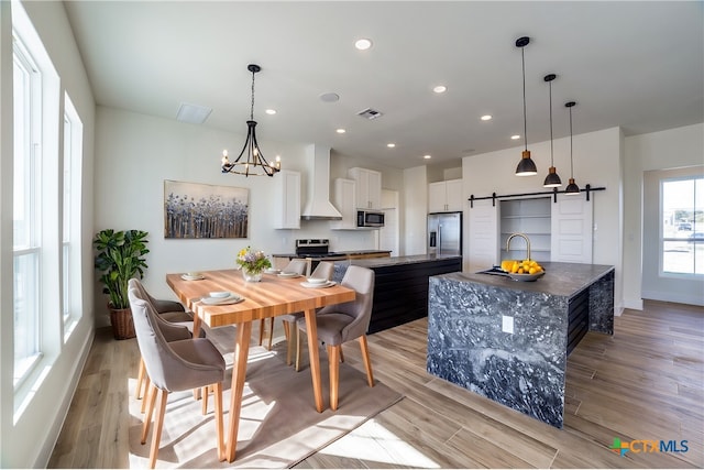 dining room featuring a barn door, an inviting chandelier, sink, and light hardwood / wood-style flooring