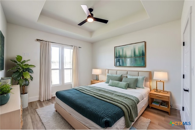 bedroom featuring ceiling fan, a tray ceiling, and light hardwood / wood-style flooring