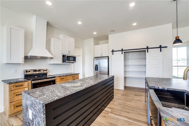 kitchen with white cabinets, appliances with stainless steel finishes, a barn door, and wall chimney range hood