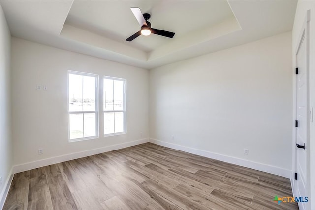 empty room featuring light hardwood / wood-style flooring, a raised ceiling, and ceiling fan