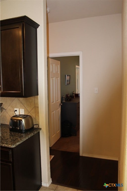 kitchen with dark stone countertops, tasteful backsplash, dark brown cabinetry, and light hardwood / wood-style flooring