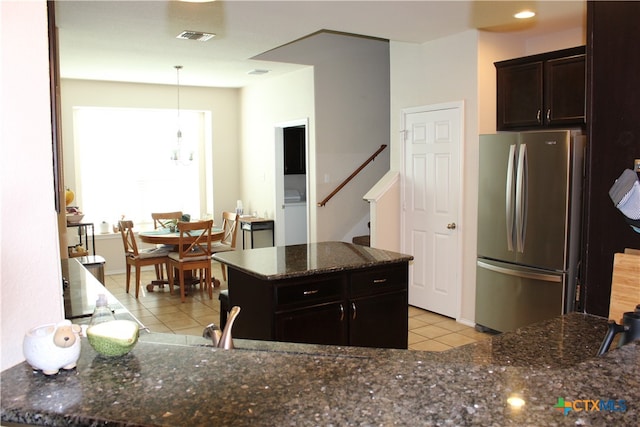 kitchen featuring dark stone counters, a kitchen island, dark brown cabinetry, stainless steel refrigerator, and light tile patterned floors