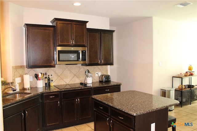 kitchen featuring black electric stovetop, dark brown cabinetry, light tile patterned floors, sink, and a center island