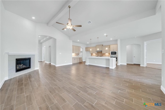 unfurnished living room with arched walkways, visible vents, light wood finished floors, and ceiling fan