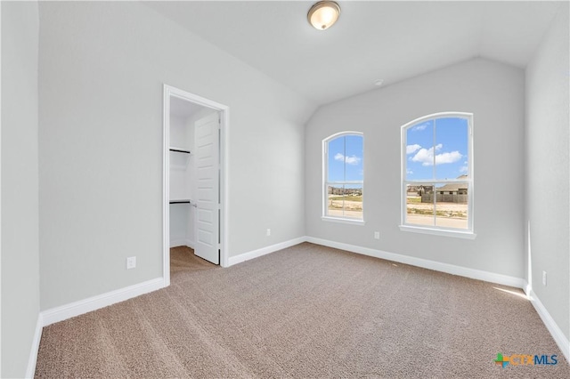 unfurnished bedroom with baseboards, carpet, a spacious closet, and vaulted ceiling