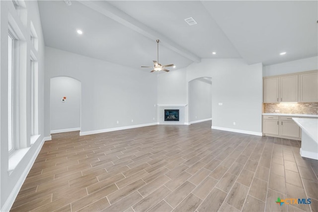 unfurnished living room featuring light wood-style flooring, vaulted ceiling with beams, arched walkways, and ceiling fan