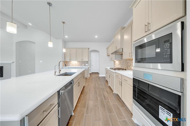 kitchen with a sink, arched walkways, appliances with stainless steel finishes, and under cabinet range hood