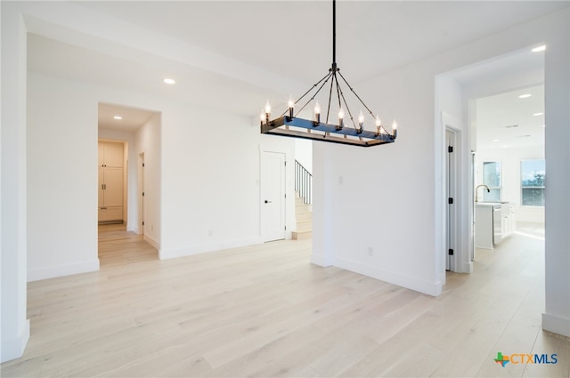 unfurnished dining area with sink, a notable chandelier, and light hardwood / wood-style flooring