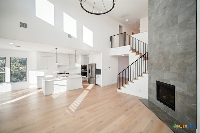 unfurnished living room with sink, a towering ceiling, a tile fireplace, and light hardwood / wood-style flooring