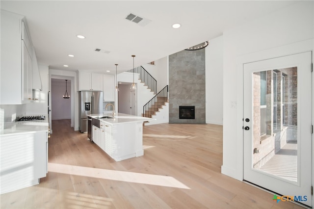 kitchen with stainless steel appliances, a center island with sink, white cabinets, light hardwood / wood-style flooring, and decorative light fixtures