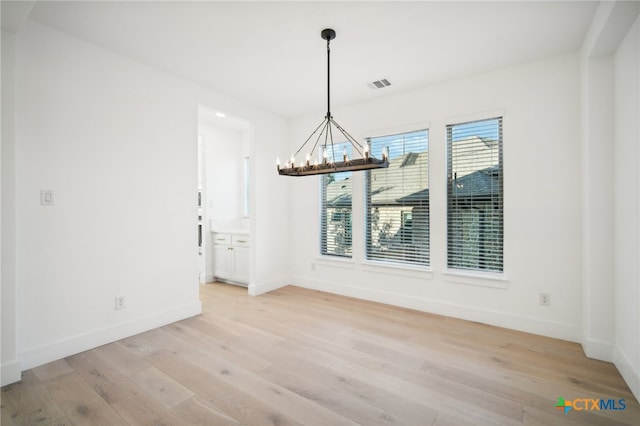 unfurnished dining area featuring light wood-type flooring and a chandelier