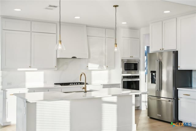 kitchen featuring stainless steel appliances, decorative light fixtures, an island with sink, light hardwood / wood-style flooring, and white cabinets