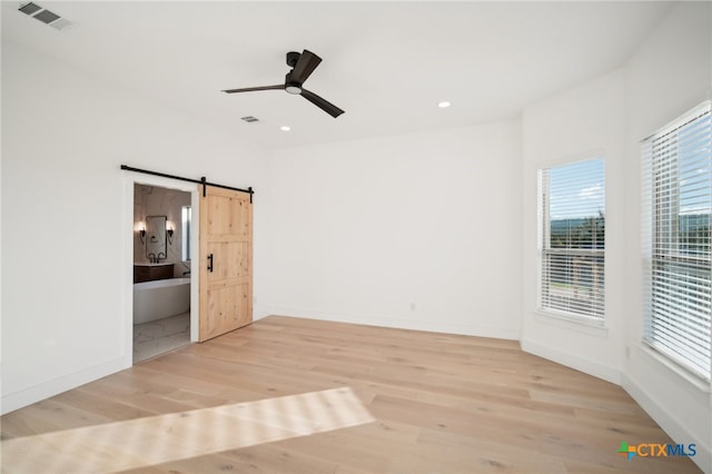 empty room featuring a barn door, ceiling fan, and light hardwood / wood-style flooring