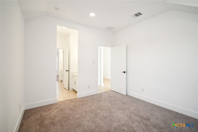 unfurnished bedroom with vaulted ceiling, light colored carpet, and ensuite bathroom