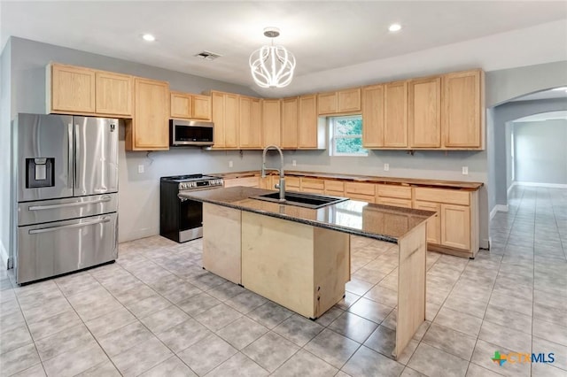 kitchen with light brown cabinetry, sink, decorative light fixtures, appliances with stainless steel finishes, and a kitchen island with sink