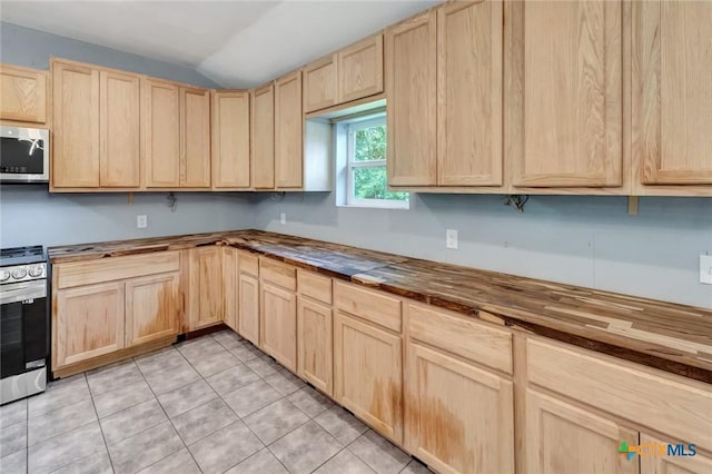 kitchen with lofted ceiling, butcher block counters, light brown cabinetry, light tile patterned floors, and appliances with stainless steel finishes