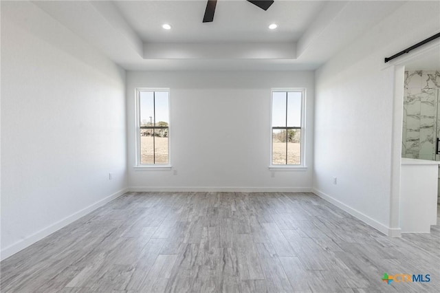 spare room featuring ceiling fan, baseboards, a barn door, and wood finished floors