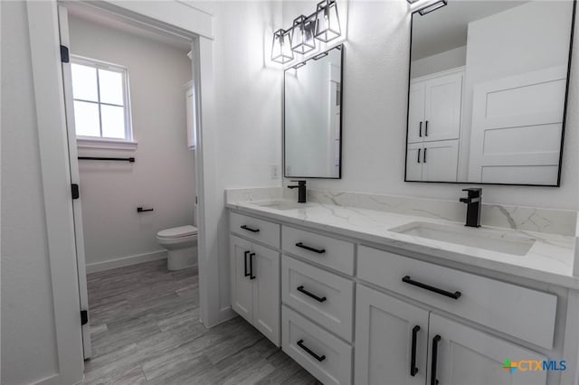 bathroom with double vanity, toilet, baseboards, and a sink