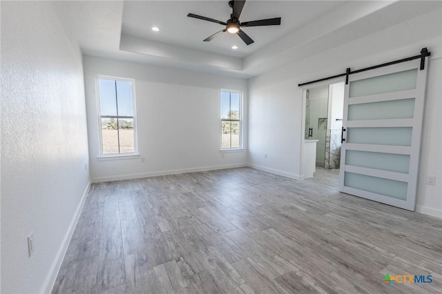 unfurnished bedroom featuring a barn door, a raised ceiling, multiple windows, and wood finished floors