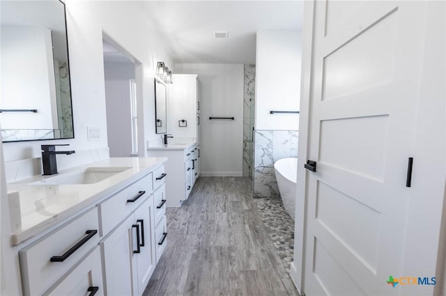 full bathroom featuring visible vents, a marble finish shower, a soaking tub, two vanities, and a sink