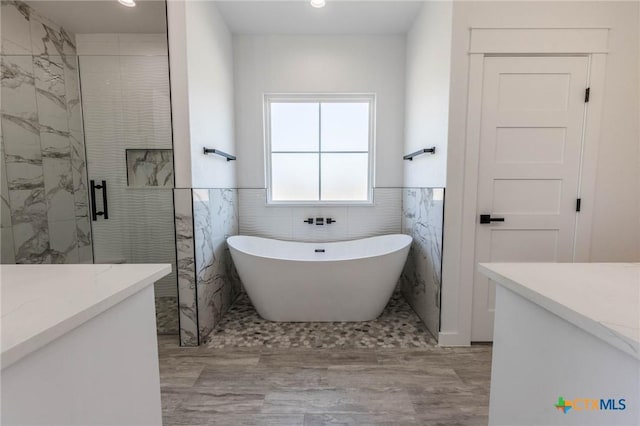 full bathroom with vanity, a wainscoted wall, a stall shower, a freestanding bath, and tile walls