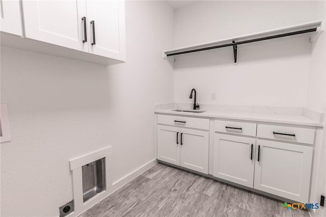 laundry area featuring baseboards, cabinet space, electric dryer hookup, a sink, and light wood-type flooring